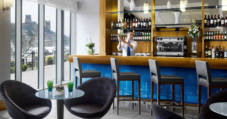 man making cocktail at bar inside Radisson Blu Hotel Durham with view of Durham Cathedral out of the window.